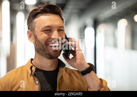 Cheerful Businessman Talking On Cellphone Looking Aside Standing In Office Stock Photo