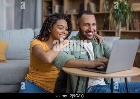 Happy african american husband and wife using laptop computer, browsing internet, resting together at home Stock Photo