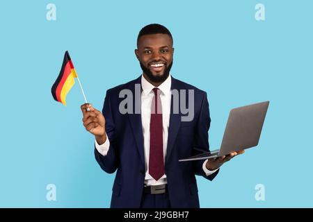 Smiling Black Man In Suit Holding Laptop And German Flag Stock Photo