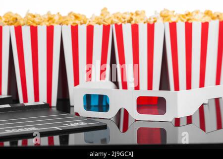 Cinema, movie, leisure and theater concept. Popcorn boxes with white and red stripes full of sweet with caramel popcorn, 3D glasses and clapperboard o Stock Photo