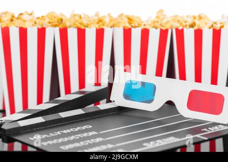 Cinema, movie, leisure and theater concept. Popcorn boxes with white and red stripes full of sweet with caramel popcorn, 3D glasses and clapperboard o Stock Photo