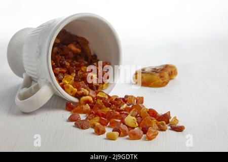 Raw amber spilled out on a wooden table from a white ceramic cup. Semi-precious rough stone Stock Photo