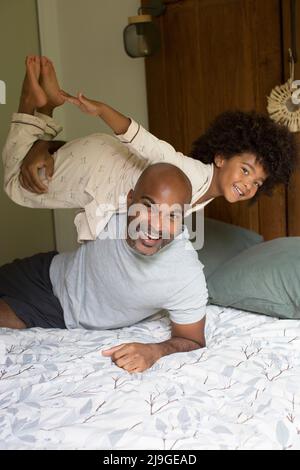 Smiling father carrying his daughter on shoulder in bedroom Stock Photo