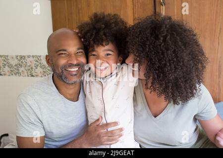 Happy parents sitting with daughter on bed Stock Photo