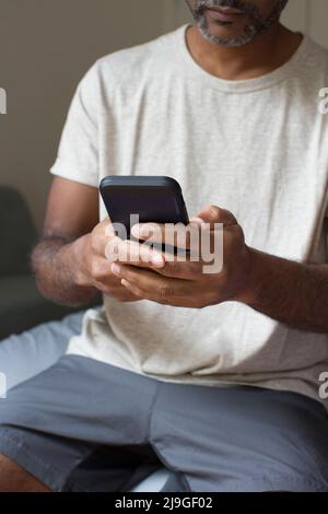 Man using smart phone while sitting in bedroom Stock Photo