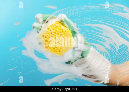 Hand in rubber gloves wipes the glass with a yellow foam sponge. Light blue background. The concept of professional cleaning service. Stock Photo