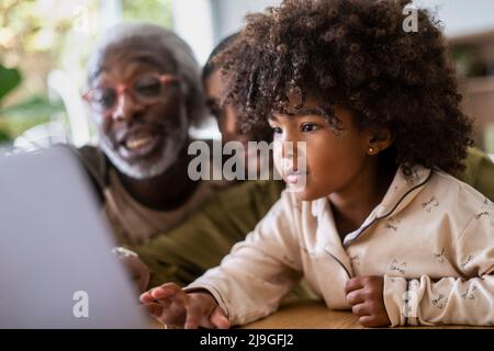 Smiling grandparents with granddaughter using laptop Stock Photo