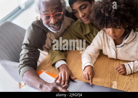 Smiling grandparents with granddaughter using laptop Stock Photo
