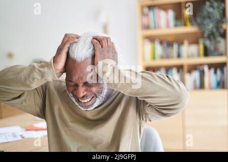 Senior man suffering from headache while sitting in living room Stock Photo