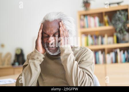 Senior man suffering from headache while sitting in living room Stock Photo