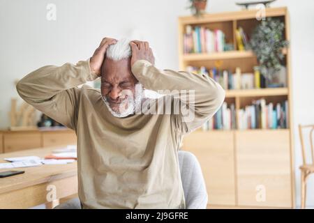 Senior man suffering from headache while sitting in living room Stock Photo