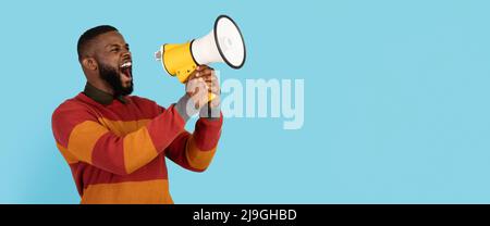 Portrait Of Young African American Man With Megaphone In Hands Making Announcement, Black Millennial Male Shouting Aside At Copy Space On Blue Stock Photo