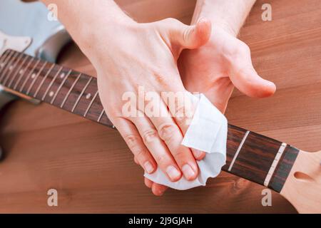 Guitar master polishing fretboard of electric guitar, close up shot of hands with cloth Stock Photo