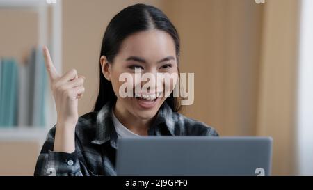Thinking student girl asian pensive woman portrait sits in front of laptop doing online task looking for problem solution feels doubtful deep in Stock Photo