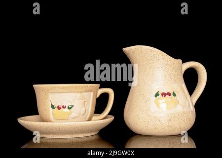 One ceramic cup on a saucer and a milk jug, close-up isolated on a black background. Stock Photo