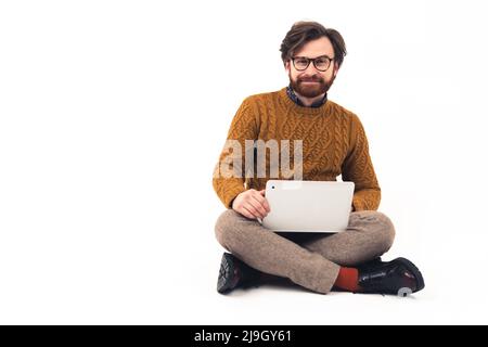 Friendly handsome unshaved millennial caucasian guy sitting in a studio with a laptop on his knees. White background studio shot copy space. High quality photo Stock Photo