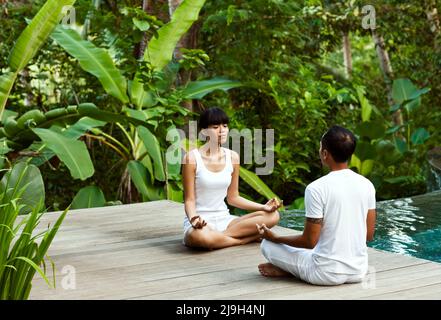 A young Asian woman meditates with an yoga  instructor in a private pool villa at Kayumanis Ubud, Bali, Indonesia. Stock Photo
