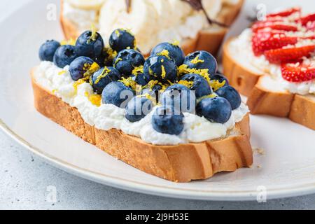 Berry vegetarian toasts for breakfast on plate, close-up. Bread slices with ricotta, berries, banana, chocolate and seeds. Stock Photo