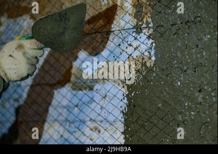 The master throws a solution of liquid concrete on the wall, the first layer of plaster on the wall, metal mesh attached to a wooden wall. Stock Photo