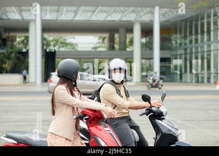 Business colleagues wearing protective helmets when riding on scooters to office in morning Stock Photo