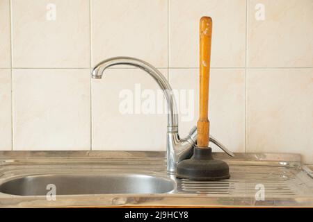 The plunger stands at the sink in the kitchen, cleaning clogged pipes, an old plunger for cleaning pipes Stock Photo