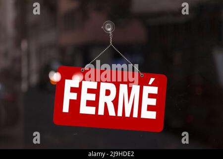 Close-up on a red sign in the window of a shop displaying the message in French - Fermé - meaning in English - Closed -. Stock Photo