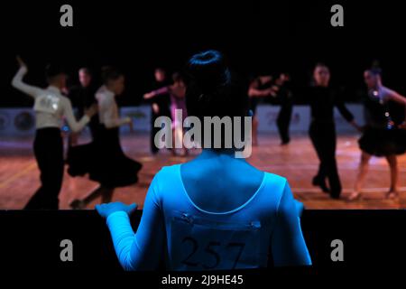 Minsk, Belarus, April 30, 2022: A little girl in a dance dress looks at the competition in dancesport. Little dancer getting ready to perform Stock Photo