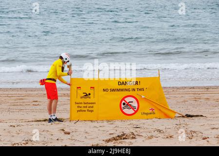 RNLI life guard erecting yellow danger no swimming banner on beach in Exmouth Devon UK Stock Photo