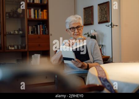 Senior woman reading book with magnifying glass at home Stock Photo