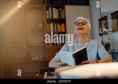 Happy senior woman with book sitting at home Stock Photo