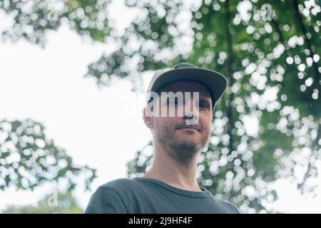 Man wearing baseball cap below tree Stock Photo