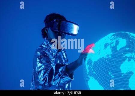 Woman wearing virtual reality simulator touching earth on screen against blue background Stock Photo