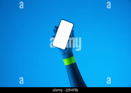 Hand of young woman holding smart phone against blue background Stock Photo