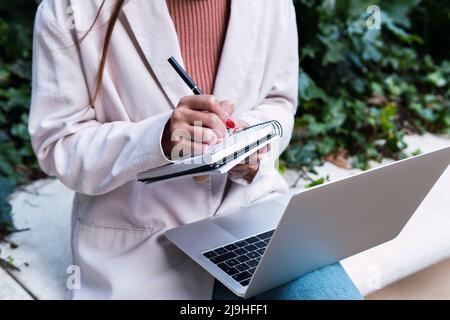 Businesswoman writing in diary sitting with laptop at park Stock Photo