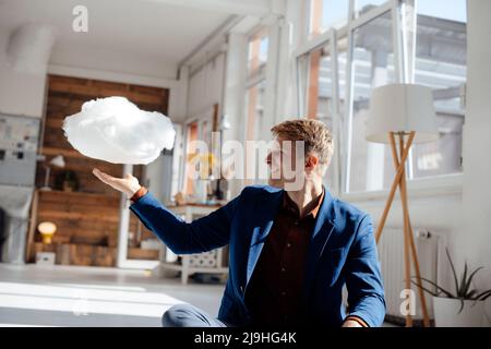 Happy businessman looking at levitating cloud network sitting in office Stock Photo