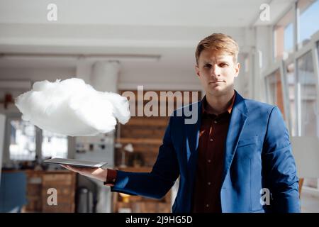 Businessman holding tablet PC under levitating cloud network in office Stock Photo