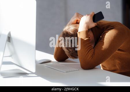 Businessman holding mobile phone sitting with hands behind head at desk in office Stock Photo
