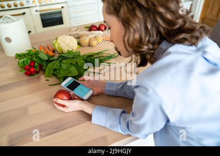 Young woman checking calories of apple on mobile app at home Stock Photo