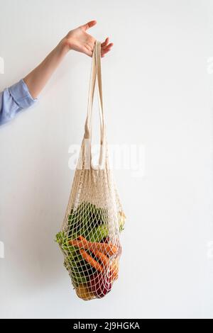 Woman holding vegetables inside mesh bag in front of wall Stock Photo