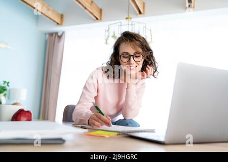 Smiling woman studying and writing in book at home Stock Photo