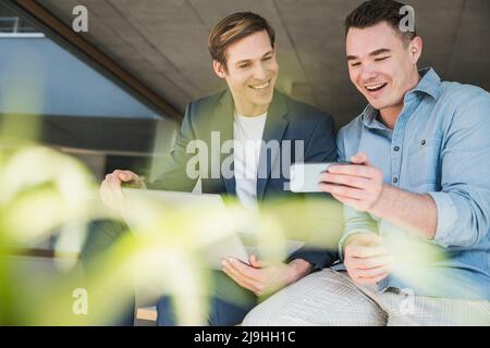 Two happy colleagues sharing smartphone in office Stock Photo