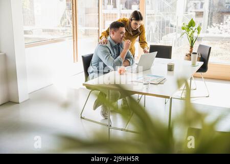 Businesswoman and businessman with laptop at desk in office Stock Photo
