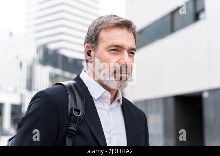 Mature businessman wearing wireless in-ear headphones Stock Photo
