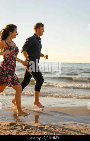 Happy couple holding hands running at beach on sunny day Stock Photo