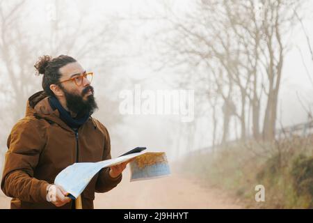 Mature bearded man wearing eyeglasses standing with map in forest Stock Photo