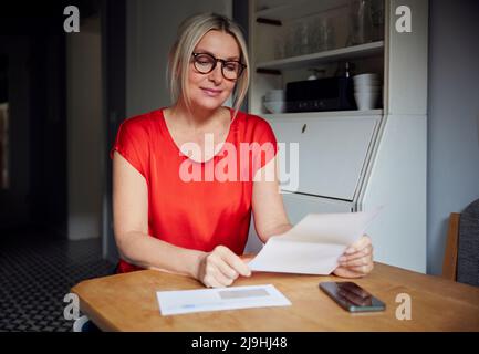 Smiling woman reading letter sitting at table Stock Photo