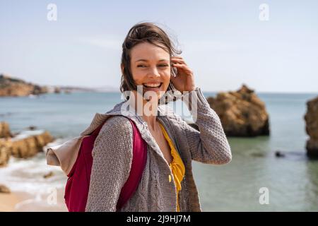 Happy woman wearing backpack standing with hand in hair Stock Photo