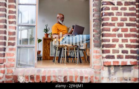 Bald man using laptop sitting on chair at home Stock Photo