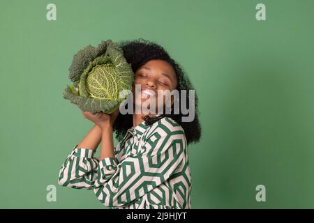 Smiling woman with eyes closed holding cabbage against green background Stock Photo