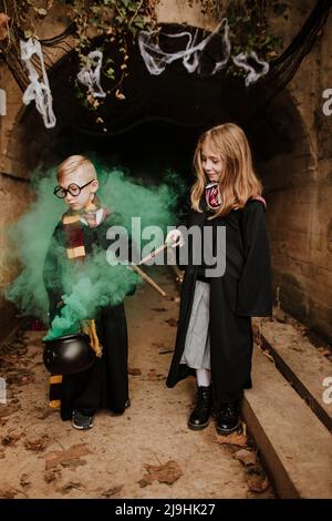 Smiling girl with brother holding magic cauldron standing in front of tunnel Stock Photo